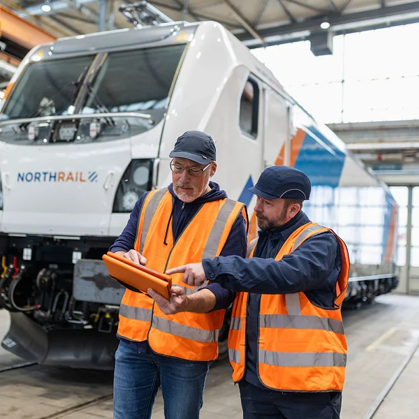 Technikmitarbeiter und Vertriebsmitarbeiter vor der Lokomotive in Besprechung am Tablet